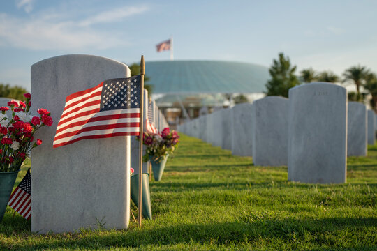 Sarasota National Cemetery with many white headstones with USA flags and flowers on green grass lawn. Memorial Day concept