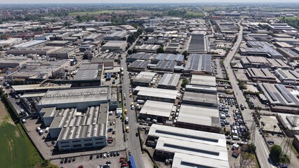 Fototapeta premium Drone aerial perspective of a suburban industrial area near Milan, Italy. Large warehouses, engineering systems, and transport routes illustrate an active logistics and manufacturing environment in Lo