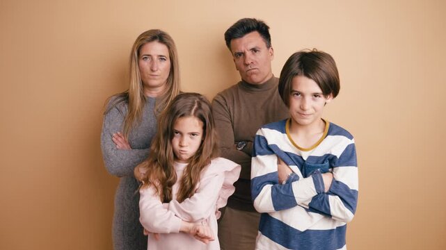 Comical family of four standing together with crossed arms and making funny, angry faces. Mother, father, son, and daughter joking around