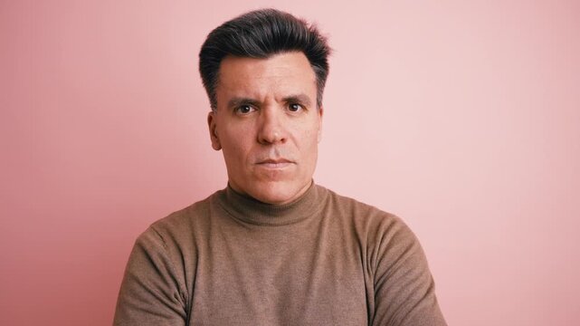 Middle aged caucasian man with an angry and disapproving expression. Serious male person staring intently at the camera on a pink background