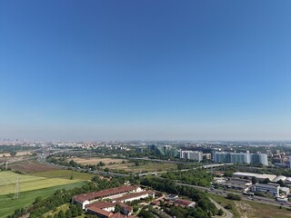 Fototapeta premium A sweeping aerial view of a bustling city stretching towards the horizon under a clear, cloudless sky. Buildings, roads, and green spaces intermingle in a tapestry of urban life.