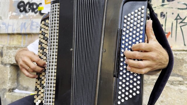 Male hands of musician playing the accordion at urban street. The detailed view highlights texture of instrument, capturing rhythm, tradition, and the expressive character of live music performance