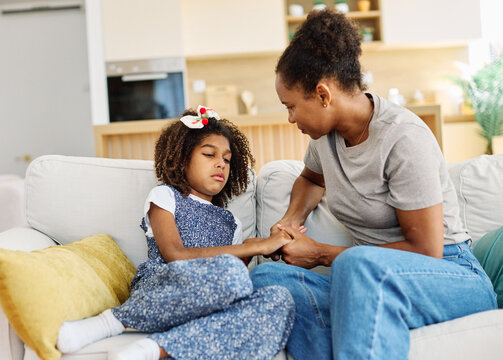 Mother embraces daughter on a couch at home while comforting her after a difficult day. Sharing secrets and problems, support and parenthood concept