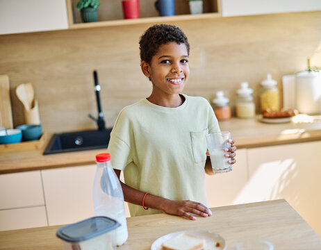 Young teen boy enjoying a glass of milk while sitting at a kitchen table  preparing for school modern kitchen