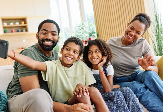 Portrait of a happy black family mother father and kids taking selfie with mobile phone having fun  at home on couch