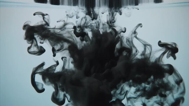 Black ink dispersing in light blue water creating abstract smoke clouds. Macro shot of dark pigment swirling underwater. Minimalist artistic background for creative video production projects.