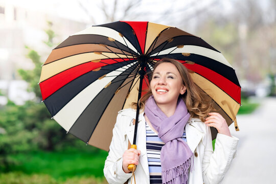 Smiling woman with colorful umbrella outdoors. Positive spring mood and refreshing walk in blooming city garden.