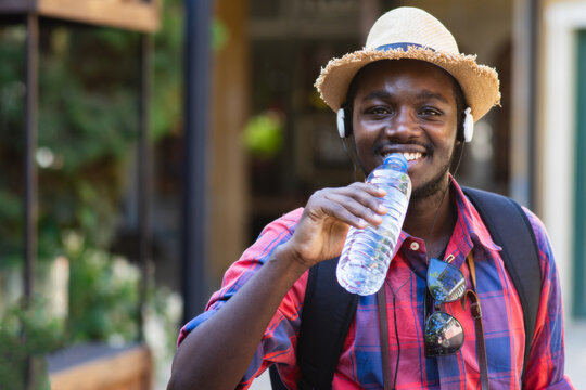 Happy African Man Drinking Fresh Water from Bottle While Traveling Outdoors