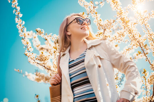 Happy woman in sunglasses under blooming tree. Joyful spring atmosphere and appreciation of seasonal renewal.
