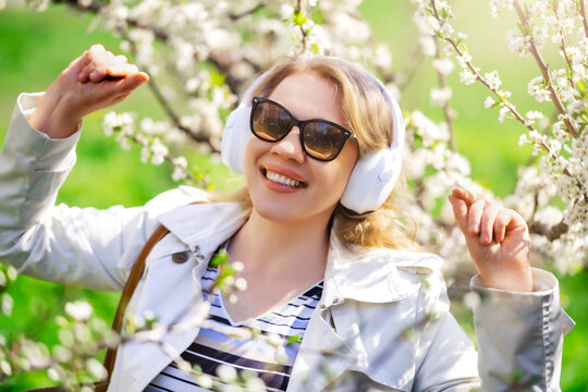 Woman in headphones dancing near flowering trees. Positive emotional expression and carefree spring energy.