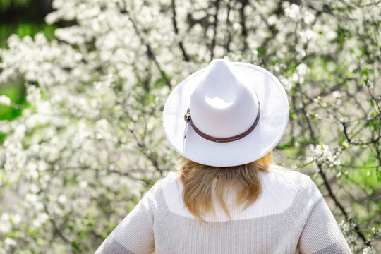 Woman in white hat near blooming trees. Simple elegance and quiet contemplation of spring nature.