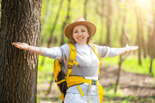 Woman with arms open near tree in forest. Freedom and connection with nature concept for mindful lifestyle