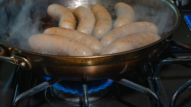 White Sausages in Stainless Skillet over Gas Burner