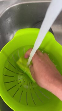 Hands squeezing soapy sponge under running water in kitchen sink