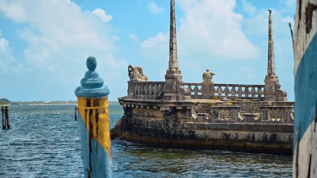 Stone barge breakwater at Vizcaya Museum and Gardens in Miami. Historic stone barge with obelisks and statues in Biscayne Bay, sunny day, blue mooring pole in foreground.