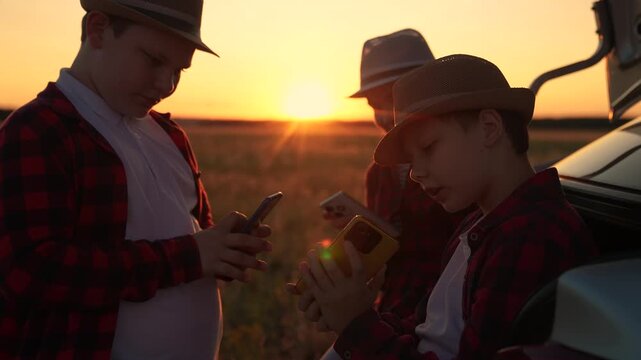 Boys, girls communicate smartphones. Children play online games on outdoors with phone in their hand next to car in nature. Children use smartphones, picnic nature, family trip. Modern technologies