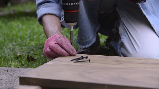 Woman using a drill screw driver on wood in an urban garden. DIY concept. Horizontal format. 