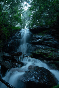 Beautiful forest waterfall cascading through a lush green forest with mist and soft sunlight filtering through the trees