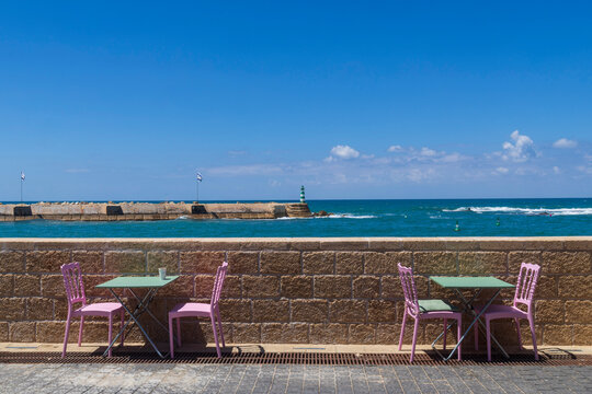 Pink chairs and green tables at an empty outdoor cafe by the sea wall in Tel Aviv. Israel