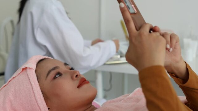 The young woman relaxes during her facial treatment. The expert's hands gently cleanse her eyes, and a soft pink towel caresses her tranquil face. Her relaxed posture conveys comfort and attentive car