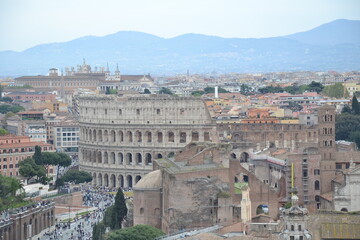 Fototapeta premium Panoramic view of the Colosseum in Rome, Italy, surrounded by historic buildings and ancient ruins under a cloudy sky. Famous European landmark and travel destination. 