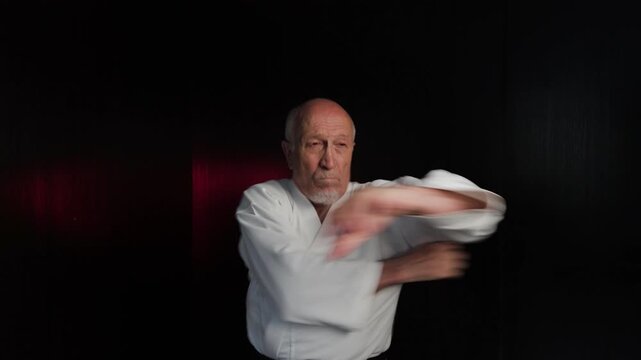Against a background of flashing red and green lights, an old male athlete throws punches and blocks with his hands