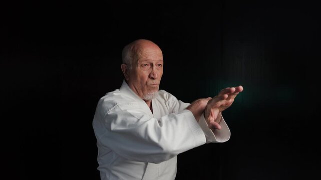 Against the background of flashing red and green lights, an old male athlete practices grabbing and striking with his hands