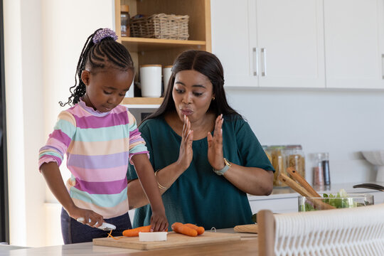 African American mom and daughter preparing carrots on kitchen island with peeler on wooden board