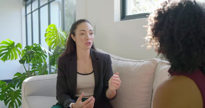Diverse women on sofa, left woman starting talk in blazer, speaking, gesturing, clarifying