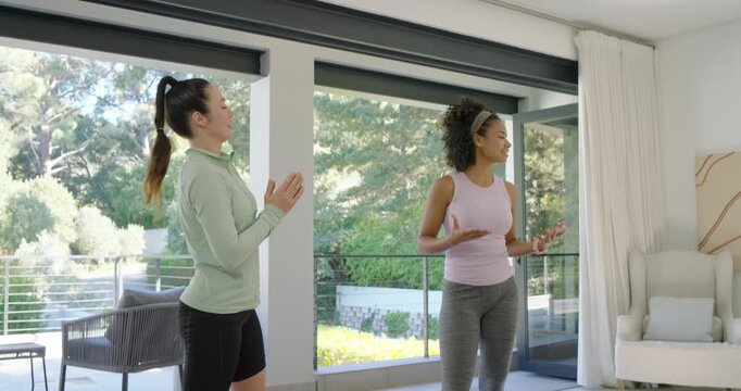 African American coach guiding Asian woman in gym gear squatting at home prepping ring light camera