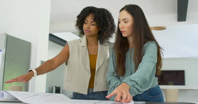 Diverse women colleagues reaching for phone, reviewing plans at white counter to finalize layout