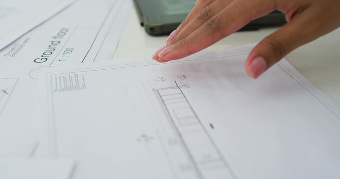 Placing finger on Ground Floor drawing, woman tracing, reviewing layout with phone near desk