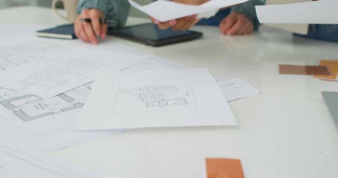 Diverse female coworkers arranging plans and planning at table with pen, right hand placing sheet