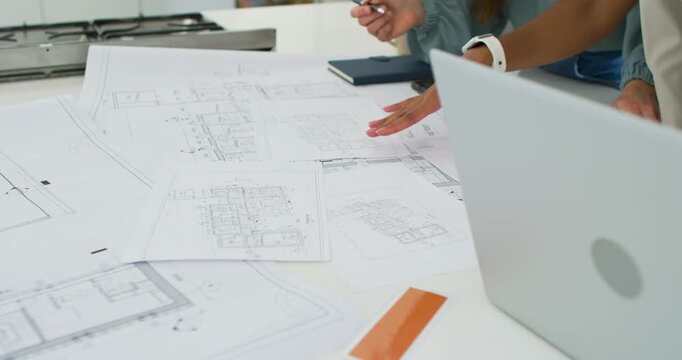 Female team working on design after opening laptop, reviewing blueprints on studio table, pointing