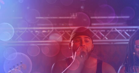 Fototapeta premium Singing mid-adult singer wearing dark tank top holding mic on concert stage, with truss and bokeh