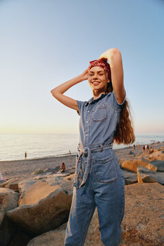 Lifestyle woman in modern boho-western denim street style poses with a red bandana by the beach at sunset in warm film color tones, expressing freedom and joy.