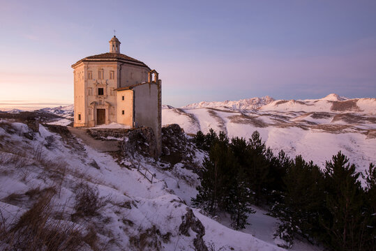 View of the octagonal Church of Santa Maria della Pieta on a snowy mountain ridge at sunset with the Apennine mountains in the background Calascio, Abruzzo, Italy.