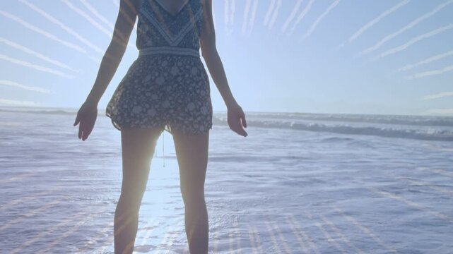 Woman standing in surf, wave splashing ankles and opening arms, sunburst overlay marking wellness