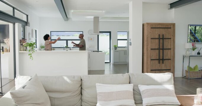 Diverse couple conversing touching hands exchanging tiny item on island moving to cabinet by sofa
