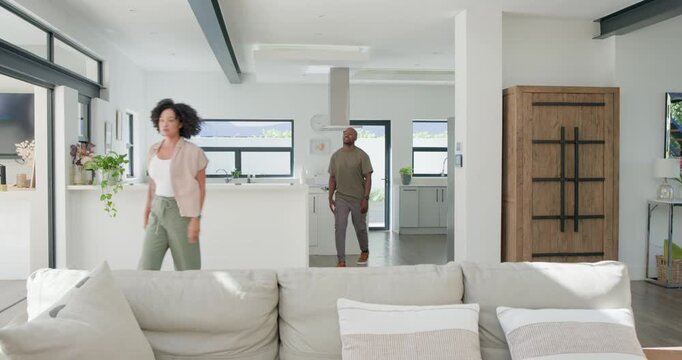 Diverse couple greeting at kitchen island, moving into living area, discussing animatedly on sofa