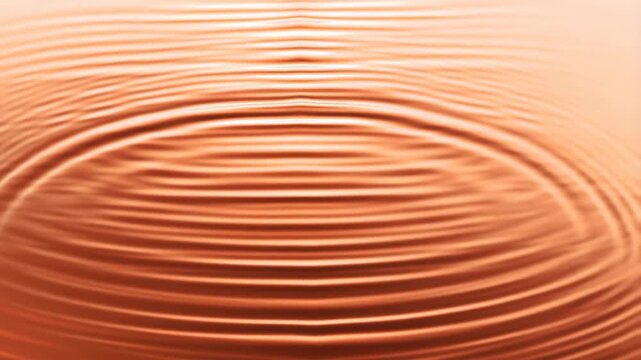 Slow motion top down static shot of concentric ripples spreading across copper colored water surface in shallow studio tank