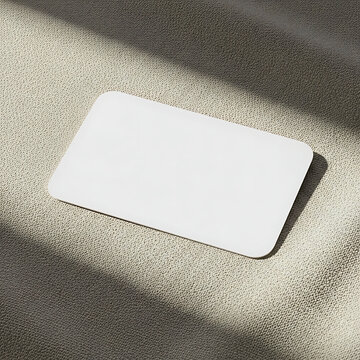 Blank white rectangular mouse pad lies on beige fabric texture background, sunlight and shadow across surface.