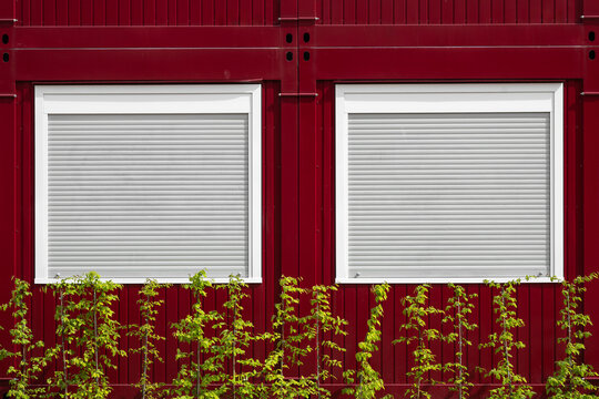 Frontal shot of a red container home with green plants in the front