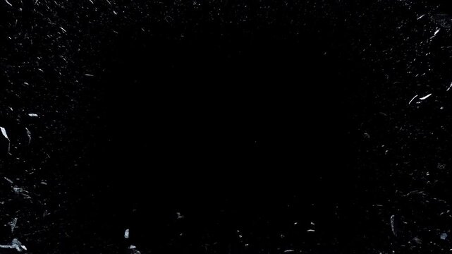 Slow motion close up of glass shards exploding and flying against black studio background with fragments and debris scattering