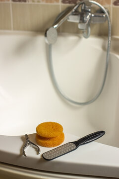 A bathroom bathtub edge with an orange sponge, a metal cuticle nipper, a foot file. Foot care kit, pedicure kit at home.