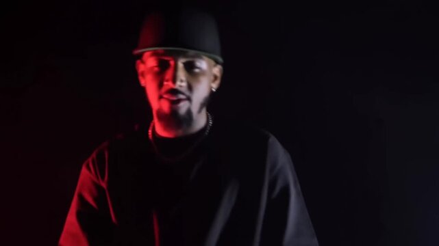 Tracking shot of male rapper performing with head nods and posing in dark smoky studio with red and blue side lighting and shadow silhouette