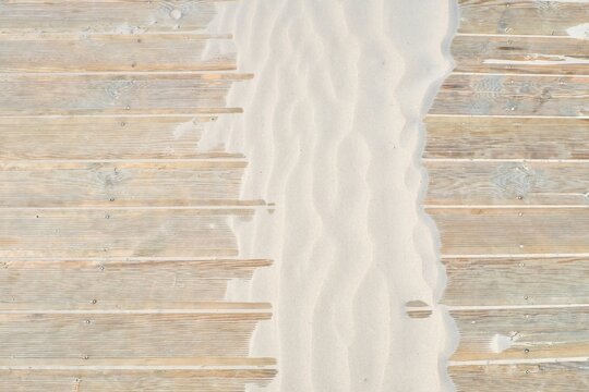 Top view of wooden boardwalk partially covered by windblown sand ripples. Minimalist beach background with natural texture of wood and sand. Summer travel, ecology and coast concept.