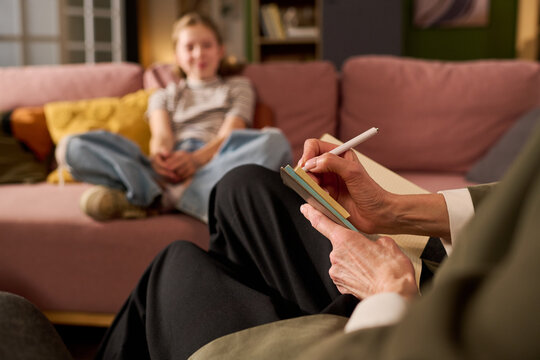 Teenage girl sitting on sofa during counseling session while therapist taking notes, representing mental health support and youth therapy. Useful for psychology, family care, wellbeing marketing