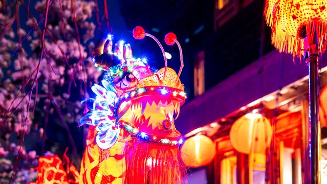 View of an illuminated Chinese dragon head with colorful LED lights and traditional lanterns at night during a festival at the Lan Su Chinese Garden in Portland, Oregon, United States.