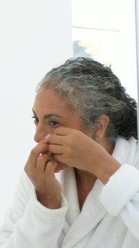 Vertical video: Holding red patch, African woman in robe applying it at vanity treating under eye